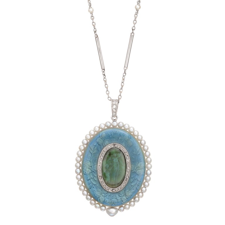 Pendant watch designed as an oval shape in blue and green enamel with small diamond accents on one side, and blue enamel with the watch dial on the other, the outer rim of the pendant lined with seed pearls, the watch powered by a mechanical