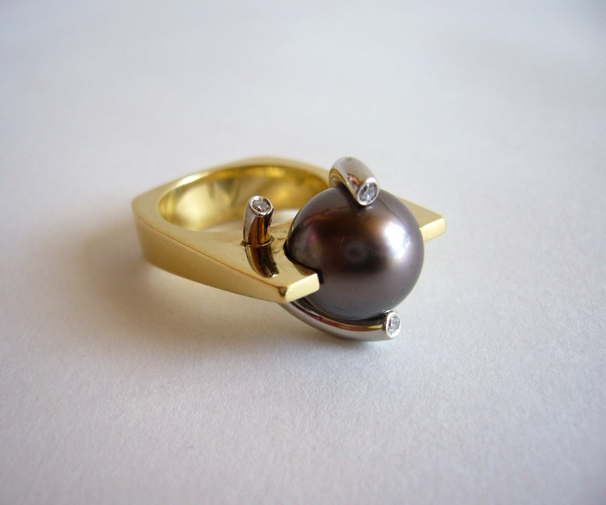 An 18k gold, platinum, diamond and Tahitan pearl ring, circa 1990's.  Ring features an 11.9 mm South Sea black pearl and four small faceted diamonds set within curved platinum rods and an 18k gold setting.  A finger size 5 3/4 and signed C & T,