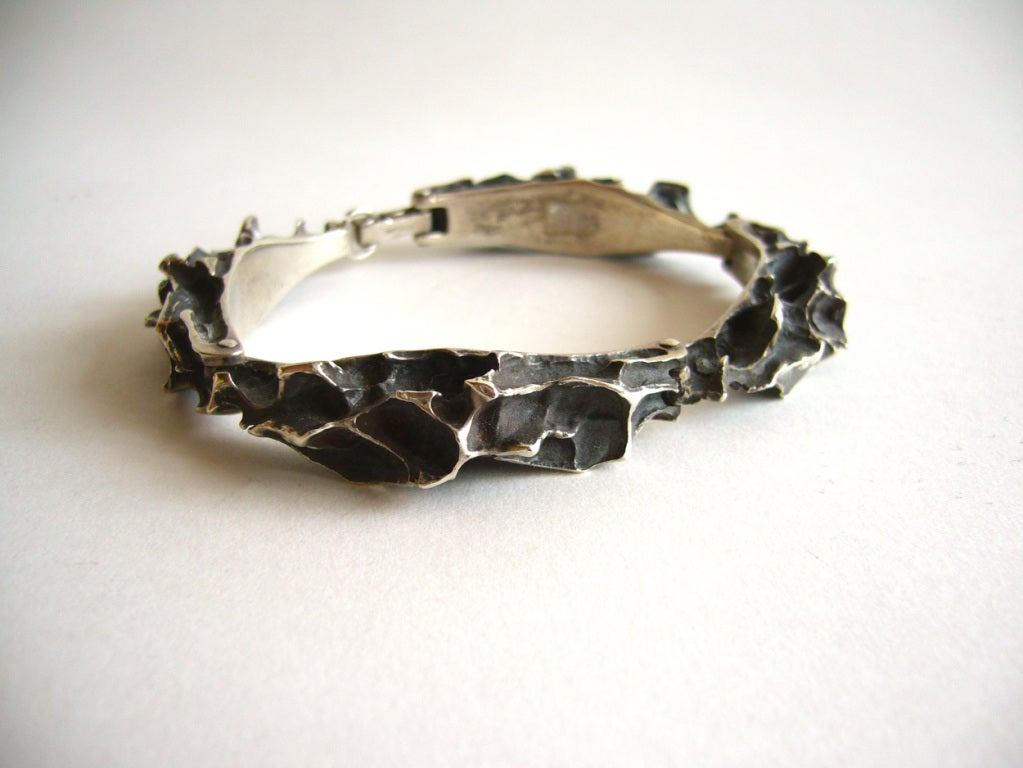 A cast sterling silver bracelet designed by sculptor Russell Secrest of Rochester New York.  Bracelet is comprised of four curved, solid silver links resembling craggy tree bark.  Its inner circumference measurement is 7