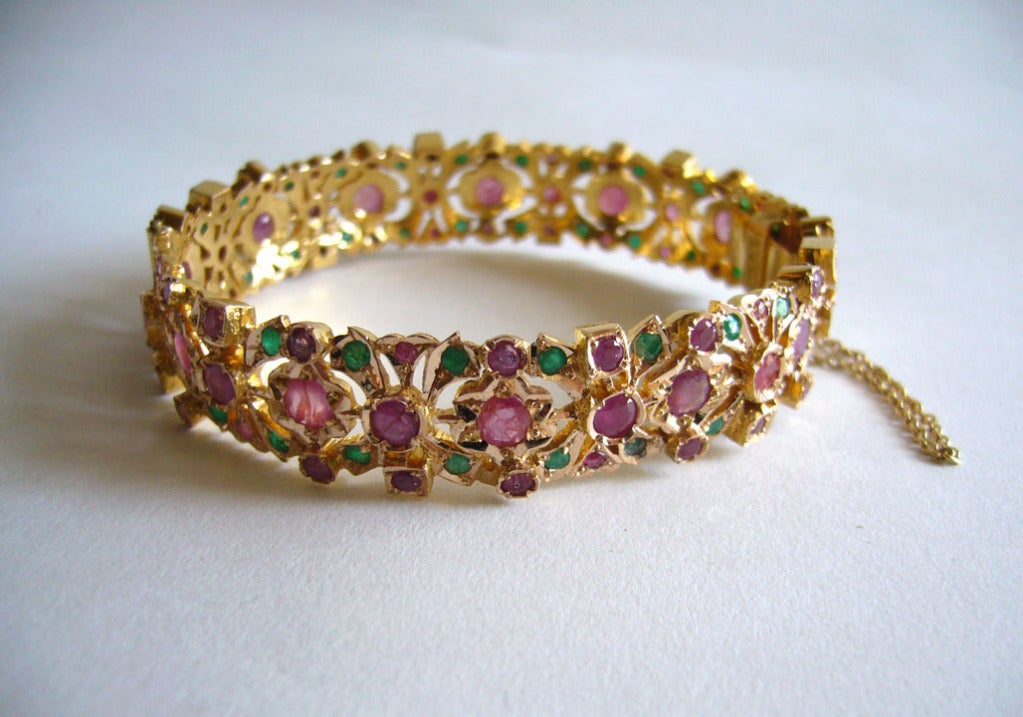 A 14 karat gold hinged bangle bracelet encrusted with rubies and emeralds.  Bracelet is 9/16