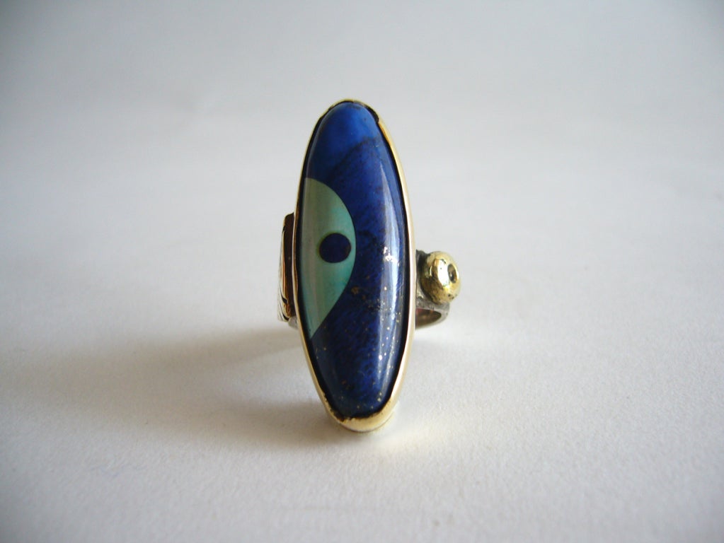 A turquoise, lapis, sterling and 14k gold ring designed by Daniel Macchiarini of San Francisco, California.  Shank has cross hatching detail and the bezel is quite unique with a cut out in its design. Ring is a size 6 1/2 and is signed Macc. In very