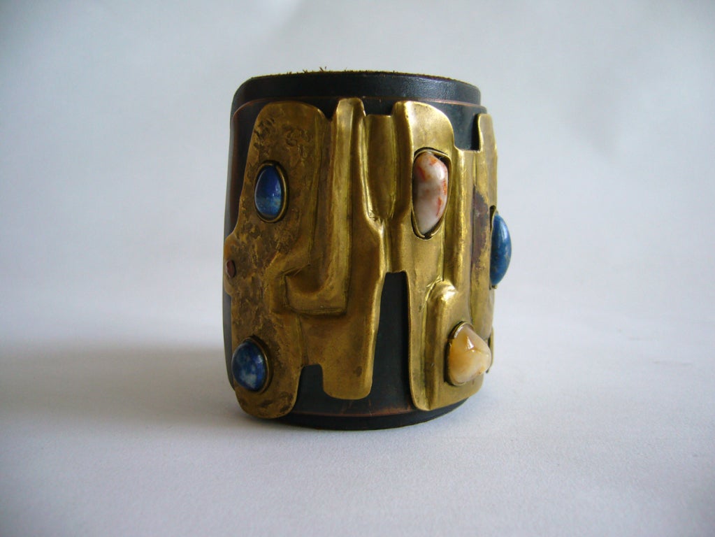 A one of a kind, handmade bracelet comprised of a uniquely hammered brass plate mounted on copper all of which is mounted onto a leather quard.  Brass features six semi precious gemstones which include lapis, turquoise and what appears to be agate