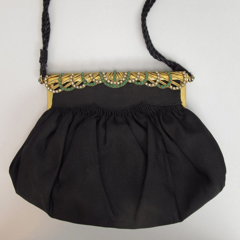 Black faille handbag with a fabulous jewel set frame. gold metal is fashioned in fan design and set with pearls and green stone cabochons, attached shoulder strap, bag is fully lined and has two interior side pockets.