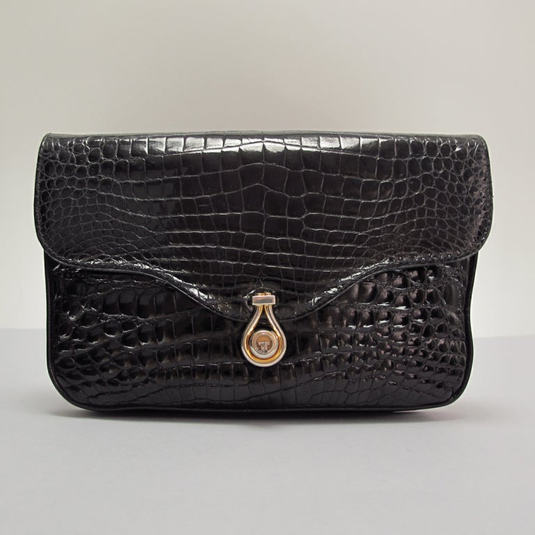 Black alligator clutch handbag from Gucci, 1970s...lined in black leather...logo snap closure in silver and gold metal...shaped flap design...two separate interior compartments and one zipper compartment at inside back and one open compartment at