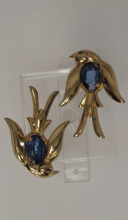 A pair of golden flying birds (pins) from Coro with large faceted blue stone bellies, one bird has a red stone eye, the other a green stone eye... approximately  2” x 1 ½” each pin.