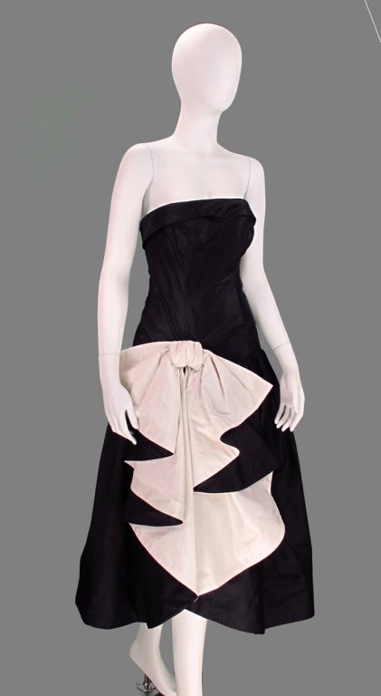 Mignon black and white cocktail dress from the 1980s...strapless design, fitted through the torso to the hip...Full gathered skirt with dramatic cascade of ruffles at the skirt front...Dress closes at the back with a zipper, bodice is boned, dress