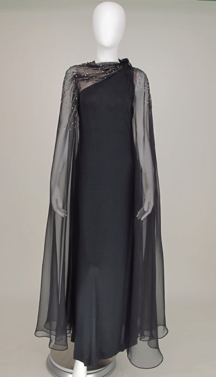 Make an entrance in this sleek, glamorous goddess style one shoulder gown...Mollie Parnis 1970s...Deep blue silk knit jersey one shoulder column gown with attached full length, sheer black chiffon open cape style sleeves...Silver bugle beads and