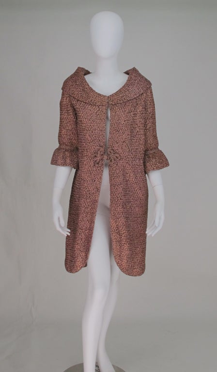 Unique lurex ribbon knit evening coat from the late 50s...iridescent pink with touches of copper and green...Shawl collar, elbow length sleeves, curved hem fronts...closes with hook/eye at collar front and with self fabric frogs at waist