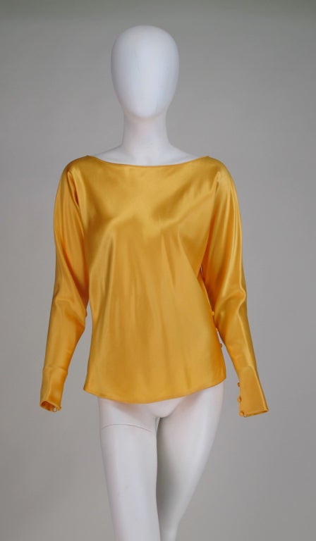 Gres Boutique saffron silk satin tunic blouse...Pull on style with bateau neckline, long dolman sleeves taper to loop and button cuffs, there are buttons and loops  at one hip side and a vent at the other, top  is fully lined in silk...Marked size