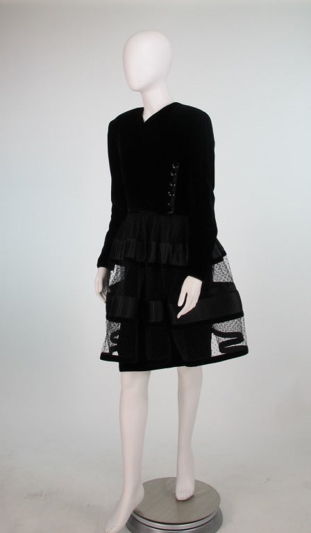 From the 1989s, Valentino black velvet & net and ribbon cage cocktail dress...Black silk velvet dress with long sleeves, V neck line, bodice has decorative side gathered & buttoned detail, shaped fitted skirt.  Attached over skirt of black point