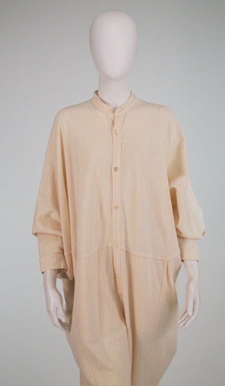Issey Miyake Plantation line...Loosely woven rough cream linen jumpsuit...Banded neck with button placket front...Angled seams create center fullness...Top stitched side front pockets...Long sleeves with banded cuffs...Full legs with banded