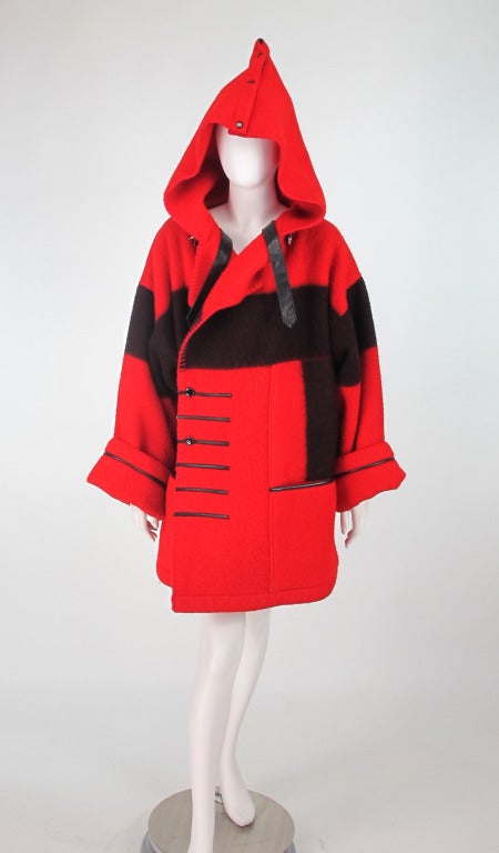 Jean-Charles de Castelbajac's take on the classic American Hudson's Bay point coat...1980s Red wool coat with a wide woven black band and black leather points at the front...There is a large collar that converts to a hood via snaps, long full