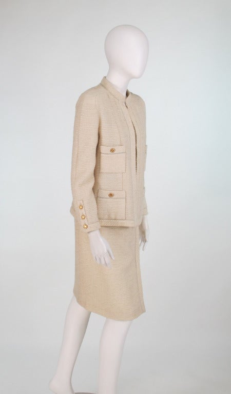 1980s Chanel ivory boucle suit with gold lurex thread...Open front suit with raglan sleeves, logo buttons at each cuff, 4 open pockets with logo buttons, weighted chain at lining hem...Skirt has wrap front, banded waist that closes with a zipper,