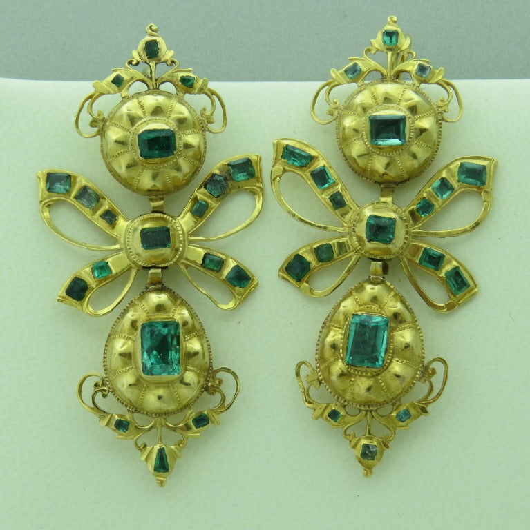 The traditional earring from Iberian Peninsula with three element design – a surmount suspending a ribbon bow which supports an elongated drop similar in shape to the surmount.  Style attributable to Spain and Portugal.

 Emeralds most likely from