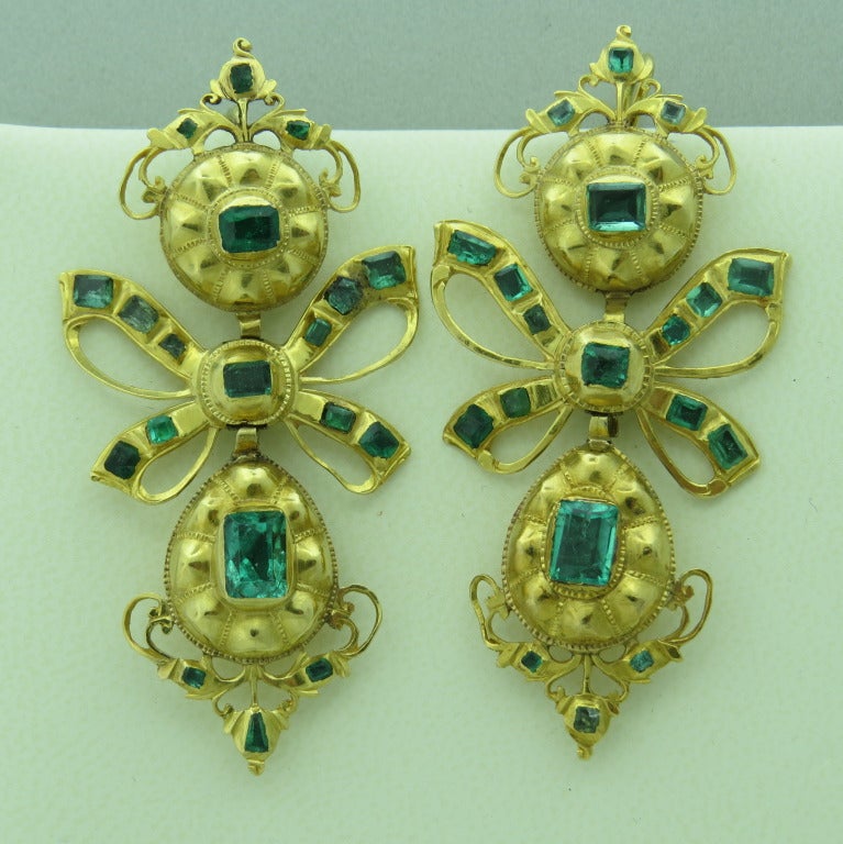 The traditional earring from Iberian Peninsula with three element design – a surmount suspending a ribbon bow which supports an elongated drop similar in shape to the surmount.  Style attributable to Spain and Portugal.

 Emeralds most likely from