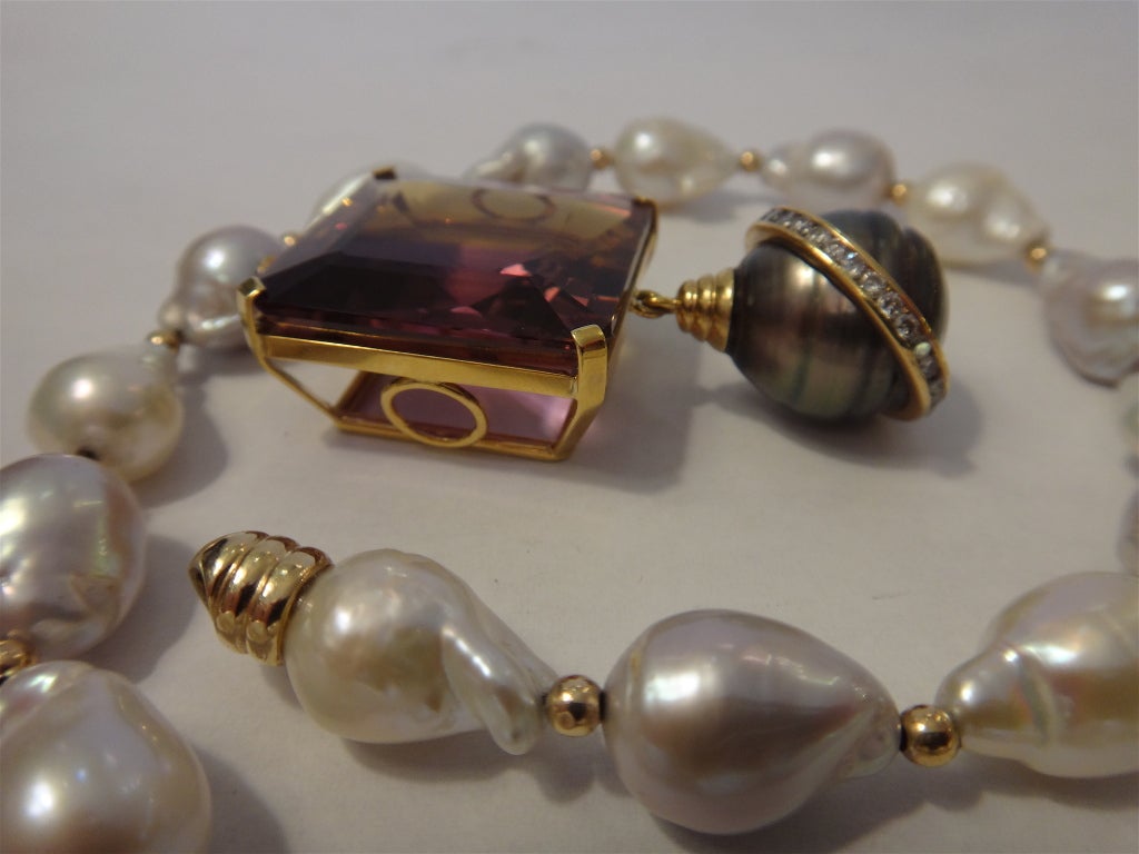 Square cut ametrine of 66 carats with a strong purple to gold color range from which is hung an 18mm baroque Tahitian pearl of medium dark color, circled by 29 channel set diamonds.  The pendant drops off a baroque pearl necklace alternating pale