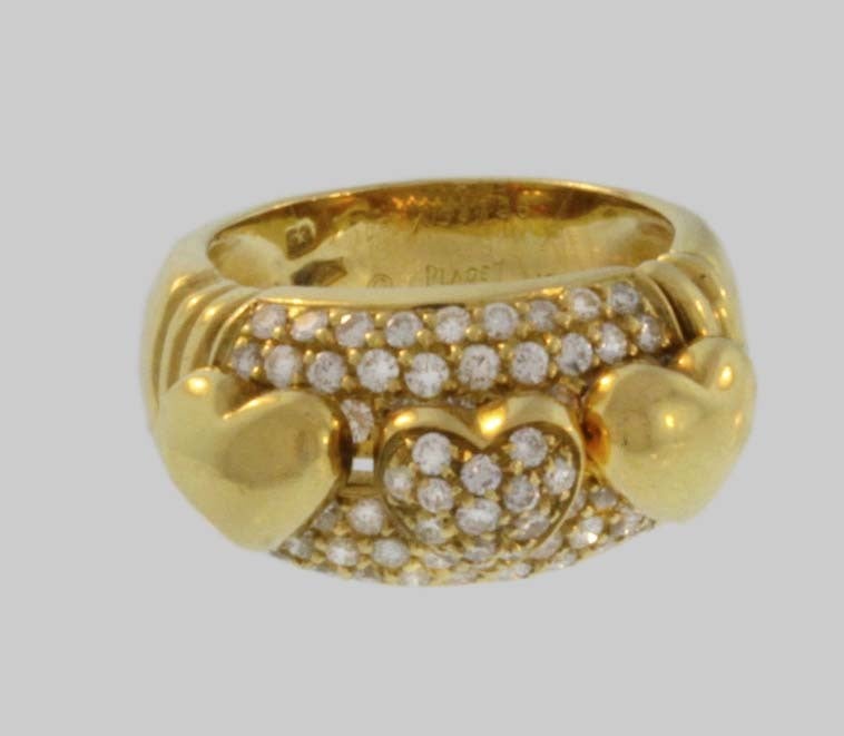 This 18K gold wide Piaget ring is inset with six rows of round-cut diamonds. Three chunky heart shapes sit atop the middle rows; the two outside hearts are gold, while the gold-framed middle one is covered with the brillaint diamonds.
