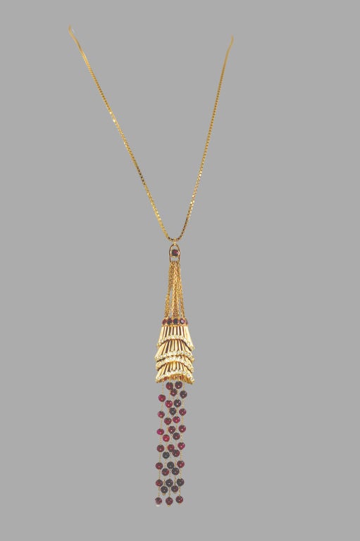 This dramatic yet playful Boucheron pendant is suspended from a cascade of 18K gold chains topped by a single, gold-encircled ruby. The chains meet a ruby-studded gold band holding multi-tiered diamond-edged, pleated gold cups from which hang