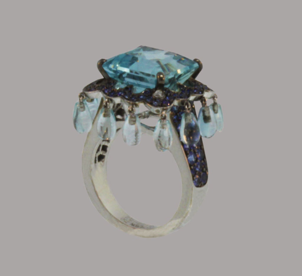 This contemporary Boucheron ring features a square aquamarine set in blackened gold. The center stone is framed by a curving row of round-cut sapphires from which dangle light-reflecting aquamarine briolettes.