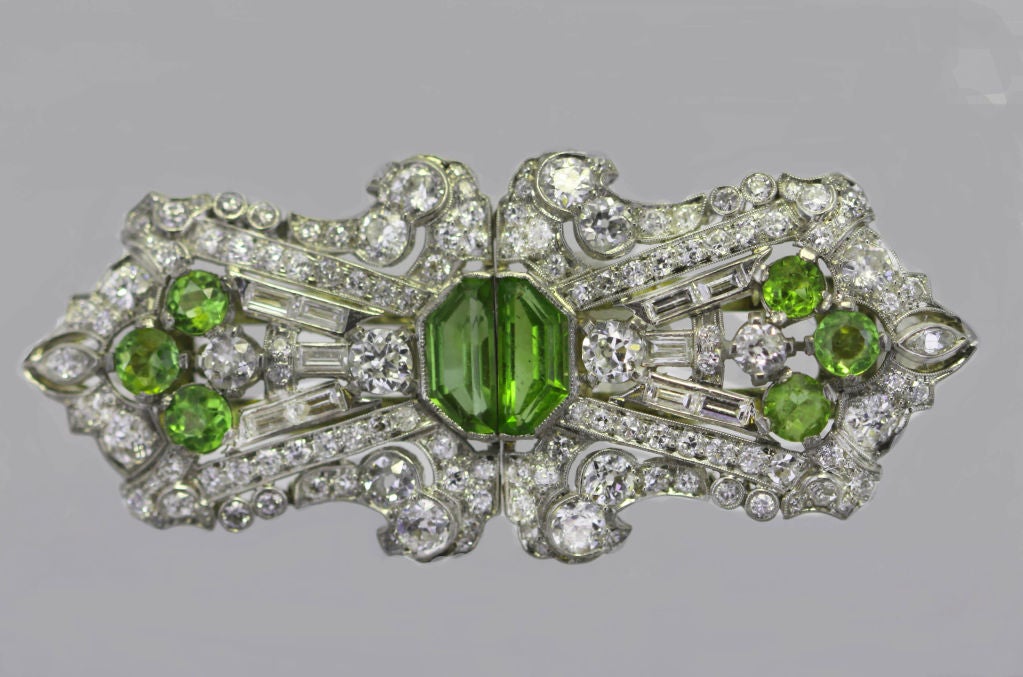 Each Art Deco dress clip of this pair is designed as an openwork geometric plaque with round and baguette diamonds, set with half-moon and round peridots. This unusual arrangement of stones is mounted in platinum.