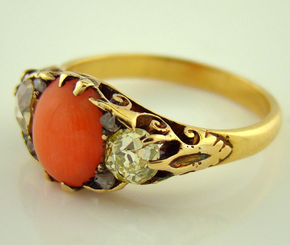 A truly charming ring, unique with the coral center in a engagement setting. This yellow gold, coral and diamond ring contains 0.75 carats of old european cut diamonds in addition to subtle accents of rose cut diamonds in between the coral and old