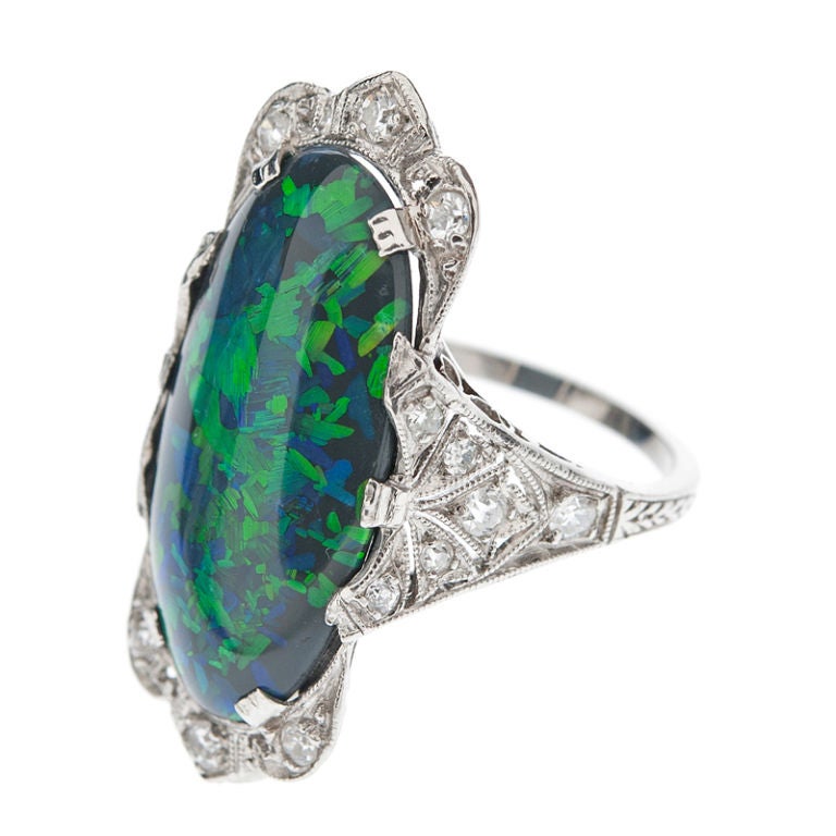 A tremendous all-original Art Deco ring, boasting a fine and scarce antique black opal. We estimate this black opal to weigh between 9.00-11.00 carats. Semi-translucent, this rare gem displays vivid colors of Green, Blue & Orange hues. Around this