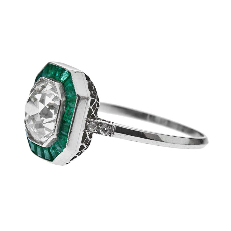 One Old European Cut Diamond weighing approximately 1.74 carats, with a color Grading of H and Clarity Grading of Vs2, is surrounded by individually hand cut and tile set emeralds creating a 