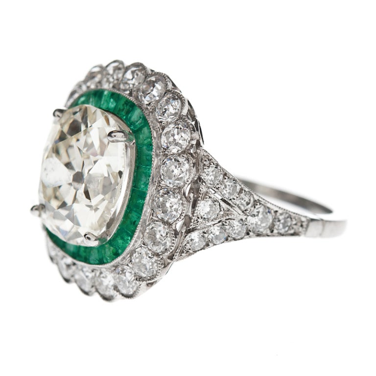 The centerpiece for this beautifully handmade platinum ring is the 4.30 carat warm fancy light yellow old european cushion cut diamond with VS1 clarity. It is surrounded by an emerald 