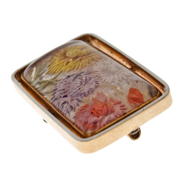 Charming and fine reverse carved brooch, depicting fluffy chrysanthemums in vibrant pastel hues, framed in a golden bezel. The center piece is then set in an outer bezel of white enamel, which makes the flowers stand out and almost