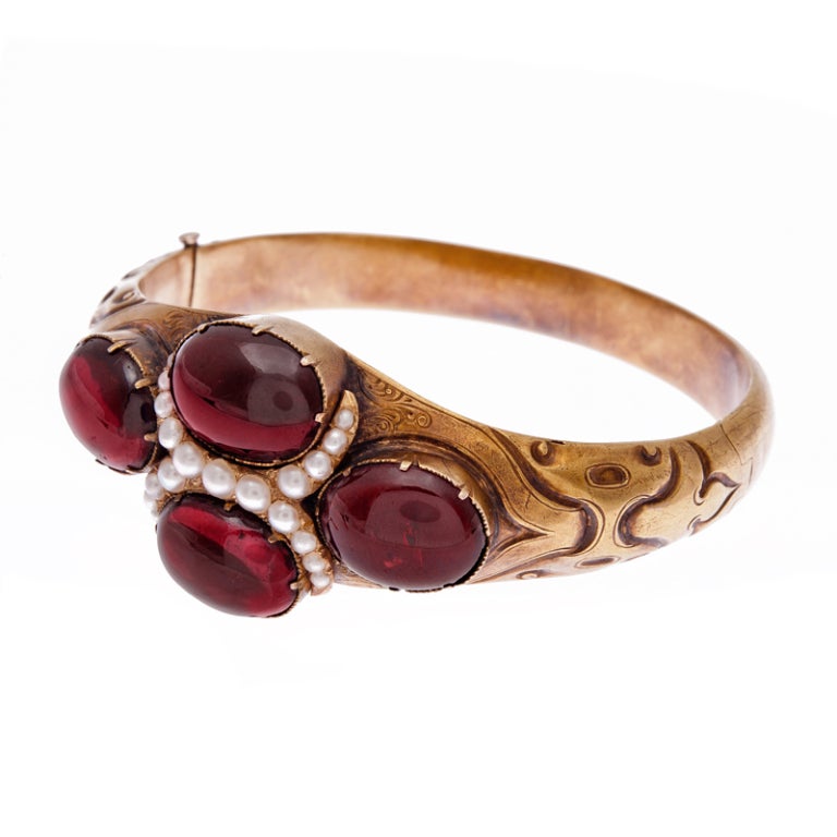Gorgeous late Victorian bangle bracelet, abundant with detail and charm, decorated with four large cabochon garnet sand a bypass style pearl centerpiece. The bracelet has one hinge and has a gentle oval shape, which fits the wrist beautifully. This