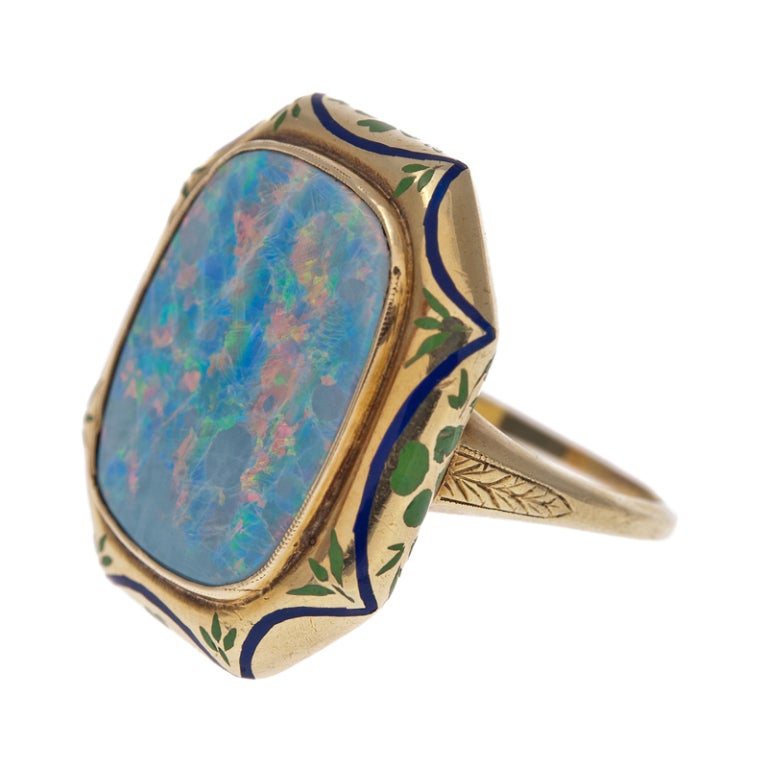 Octagonal plaque ring with a scalloped border of royal blue enamel surrounding a large oval opal. The opal exhibits strong flashes of blue and green, with modest hints of orange and red undertones and measures 18 x 15 millimeters. It is protected in