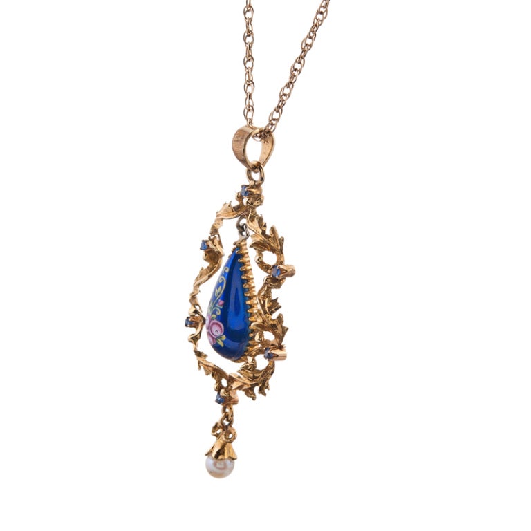 Beautiful and feminine antique pendant with a twisted frame of golden leaves with a sweet pearl suspended from a bow at the bottom. The centerpiece, an enameled teardrop with finely detailed floral design. Sapphires and diamonds are scattered