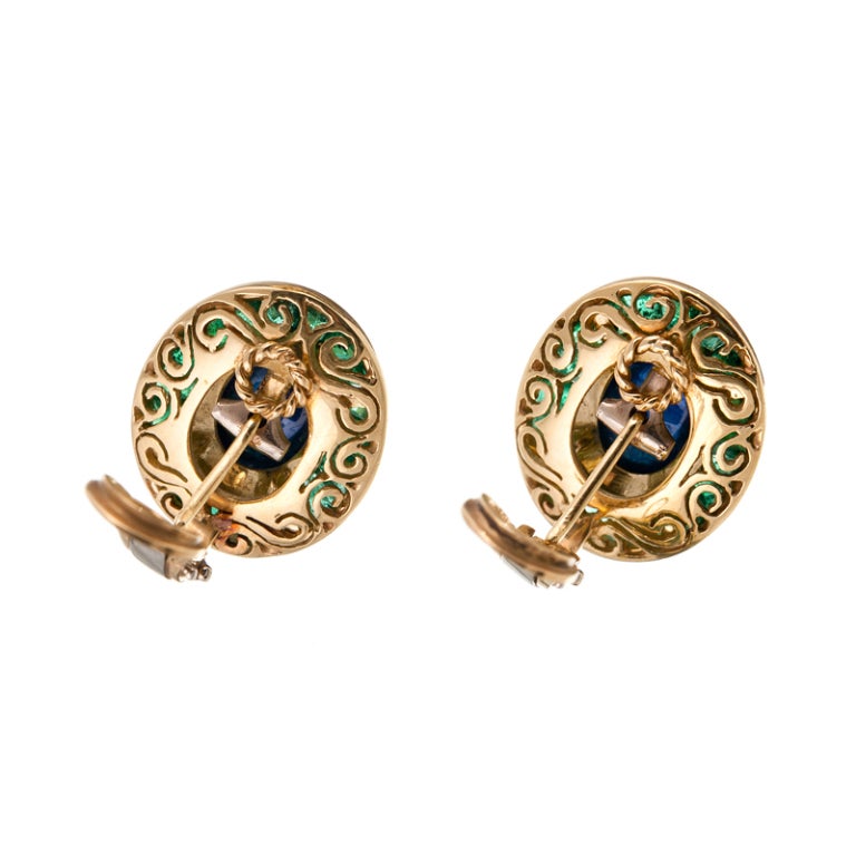 In bold contrast to one another, rich cabochon sapphires are highlighted with a precision set halo of bright emeralds. Contained in polished golden bezels, allowing the beauty of these fine colored stones to be enhanced by their shiny frames. 

In