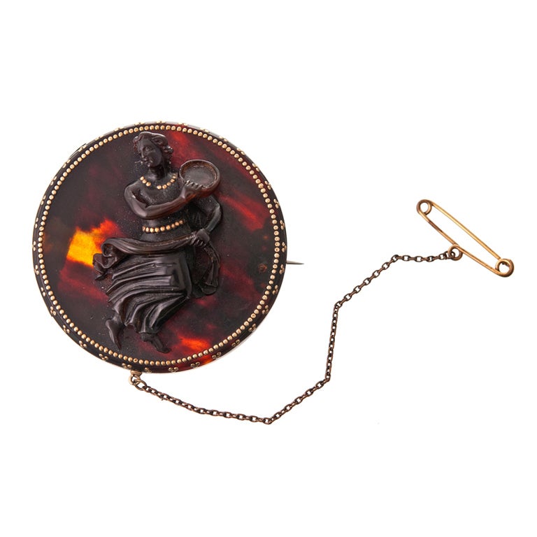A particularly nice example of a tortoise shell pique brooch, with a raised dancer, swishing her skirt in time as she plays her instrument. Bits of yellow gold are inlaid into the tortoise shell to form a gleaming border and frame, as well as adding