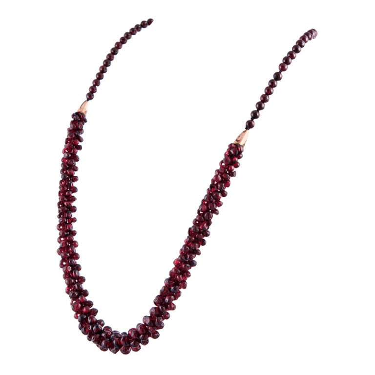A single row of round garnet beads at the top half and finished with a cluster of off-round garnet beads, fashioned into a top at the bottom. Finished with a garnet-set clasp and rose gold-toned cones connecting the sections. 21 inches in overall