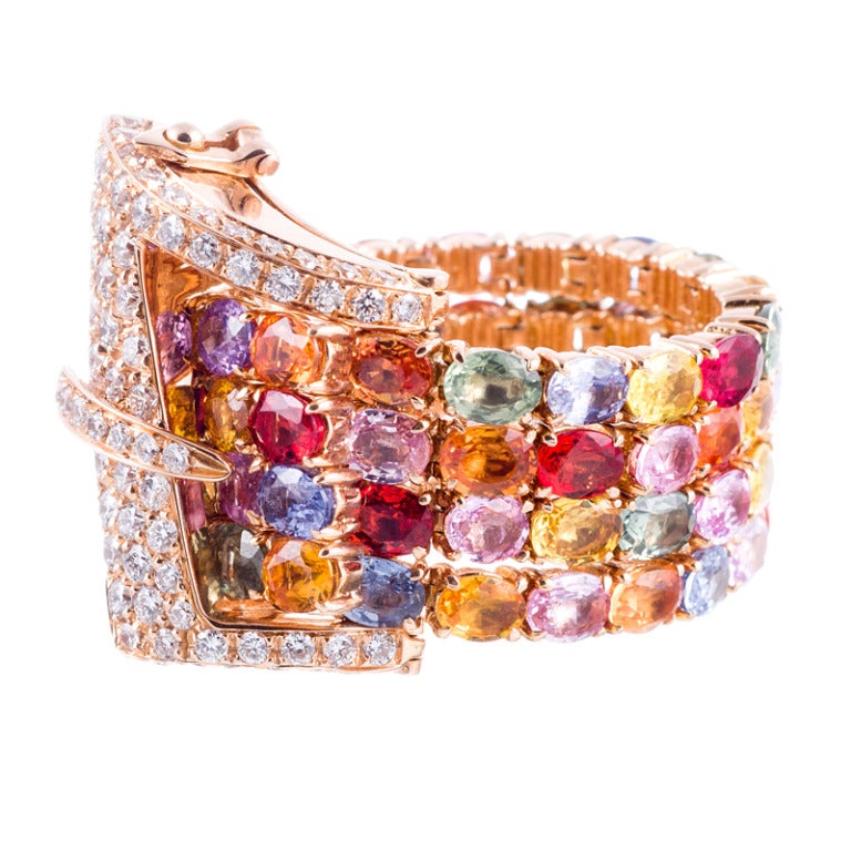 Genius: 18k rose gold buckle ring decorated with 16 carats of vibrant, multi-colored sapphires and finished with a 1.15 carat diamond buckle. This ring 