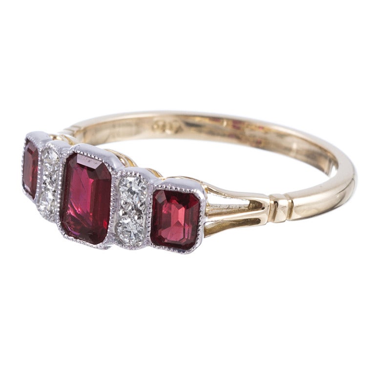 ring aus 18 Karat Gelb- und Weißgold:: besetzt mit drei Rubinen im Smaragdschliff und vier runden Brillanten. Das Design ist detailliert und doch schlicht:: mit einem schönen flachen Profil und Mille-Grain-gerandeten Lünetten:: die die Steine vor