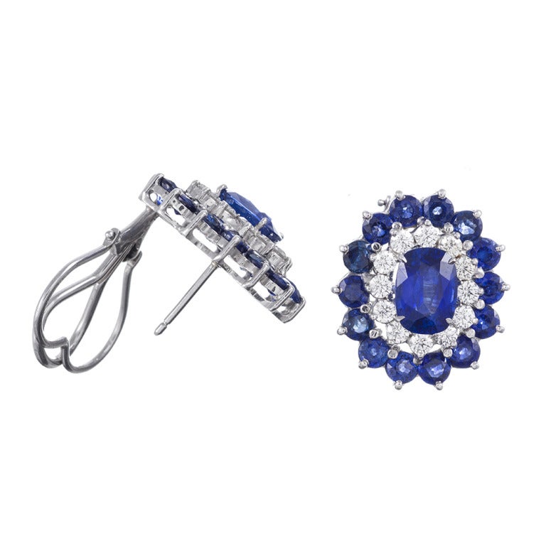 Platinum earrings, set with a 2.5 carat oval sapphire at the center of each, plus an additional 6.02 carats of round sapphire accent stones in total. Complimented by 1.20 carats of white diamonds. FInished with a post and flip-up 