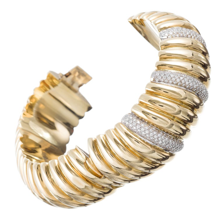 This textured oval bangle bracelet is striking, sophisticated and entirely chic. Smooth on the inside, with a 2.75 by 2 inch interior diameter, the outside is designed as a rippling ribbon of 18k yellow gold. The open and close with a single hinge