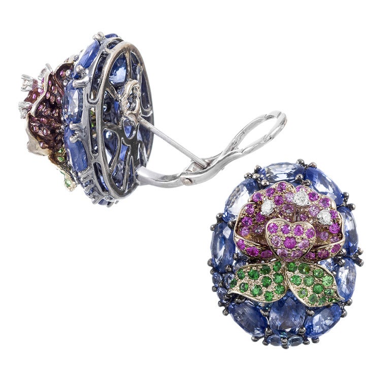 Measuring 1 inch by .75 inches and rising a half inch off the ear, these earrings are an architectural triumph of gemstones. Set in 18k white gold, on a background of mosaic cornflower blue sapphires, with a pink sapphire and diamond flower finished