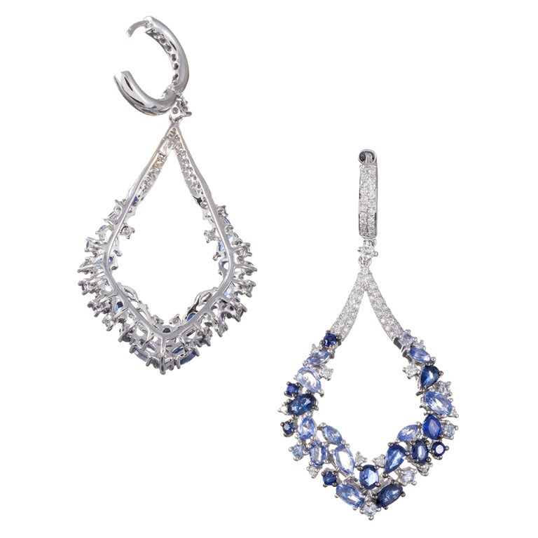 Measuring 2.25 inches in overall length, these earrings offer a miriad of blue sapphires, assorted hues and shapes artfully positioned together and fashioned ingot a modified hoop shape. They are crafted of 18k white gold and contain 7.23 carats of