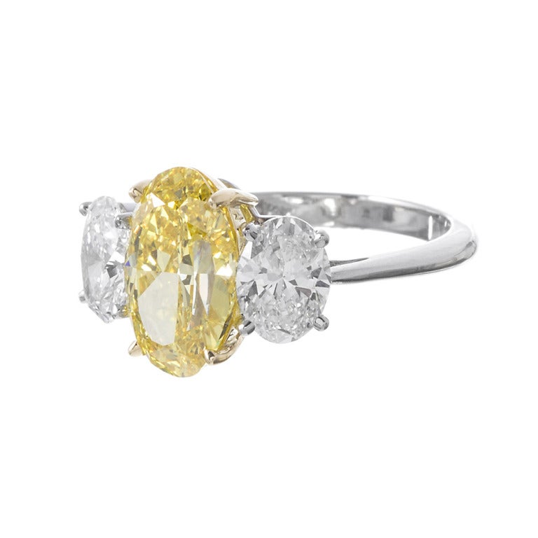 Stunning classic set with the finest and most rare color grade of natural yellow diamonds, a GIA-certidfied fancy vivid oval diamond of 2.42 carats, flanked by a pair of E-F color, Vvs clarity oval white diamonds weighing 1.50 carats in total.