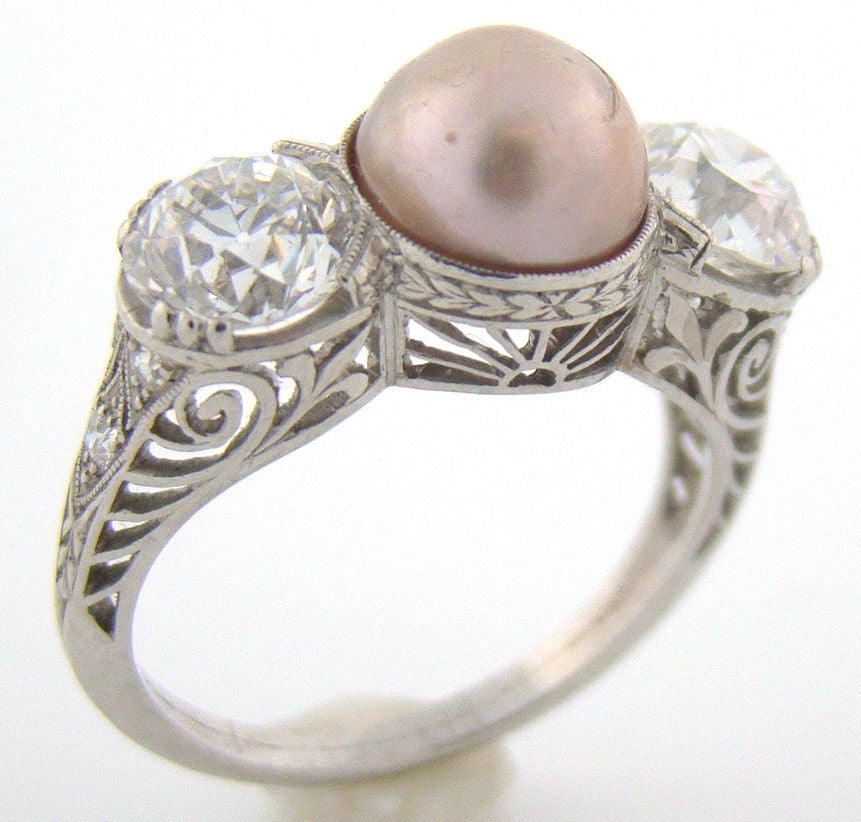 The 7.8 mm natural Pearl has a beautiful mauve luster. Flanked by two H color VS1-2 clarity Old-European-Cut Diamonds weighing a total of 2 carats. The beauty of the hand crafted filagree mounting underscores the creativity of the jeweler. A truly
