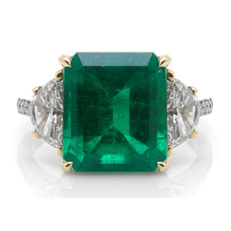 This 7.07 carat impressive emerald is a most beautiful shade of true Columbian emerald green. Two half moon diamonds, weighing 1.5 total carat weight, flank the center stone with the shanks complimented by 16 round cut micro-set diamonds totaling