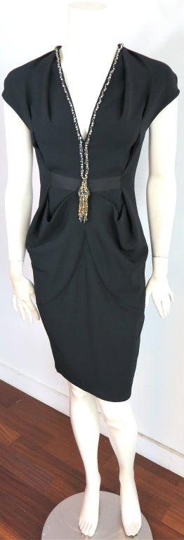 MOSCHINO draped black dress with embellished tassel necklace effect.  Embellishments are placed down the front neckline punctuated with loose tassel jewelry.  Draped effect at sides of waist.  Grosgrain ribbon detail at waist.