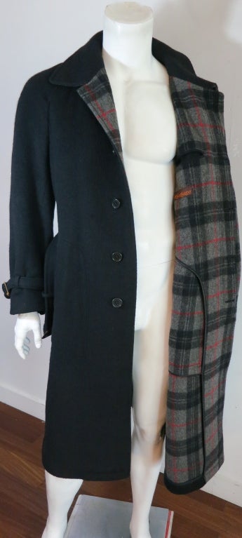 Vintage YVES SAINT LAURENT 1970's men's black coat with plaid inside face, front lapels, and under collar detailing.  Matching waist and cuff belts with leather bound, adjustable buckles.  Dual, waist level pockets with single, back vented