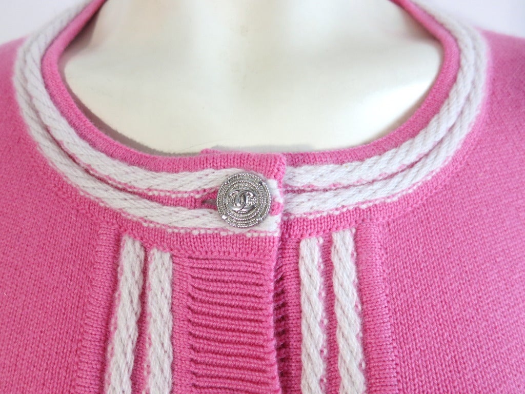 Beautiful CHANEL PARIS 100% Cashmere pink & ivory cardigan.  Knit braided effect detailing with logo engraved metal button closures.  Dual chest level pockets with wide rib construction at waist, cuffs, and front placket. Fully fashioned at