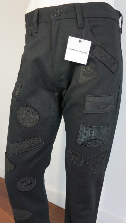 New with tag JUNYA WATANABE Comme Des Garcons motorcycle patch pants featuring Triumph, Bel Ray, Koni, and other racer themed embroidered patches.

Black on black, tonal dyed to match effect.  

Calvary cotton twill base