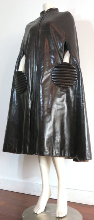 Vintage PIERRE CARDIN circa 1966-1969, dark brown PVC circle pocket cape.

This iconic, PIERRE CARDIN cape features twin, horizontal topstitched circle pockets at the front, beneath the arm opening slits.  The arm opening slits have a triangular,