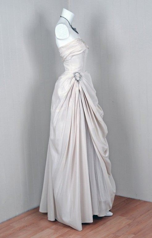 In this gorgeous 1950's ivory-white gown,the detailed construction and meticulous attention to detail are comparable to what you will find in modern haute-couture. This enchanting garment is fashioned from mid-weight taffeta and net-tulle. The